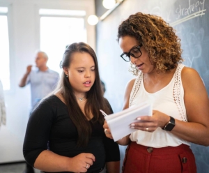 Woman in red skirt and white shire showing notes from paper to younger coworker