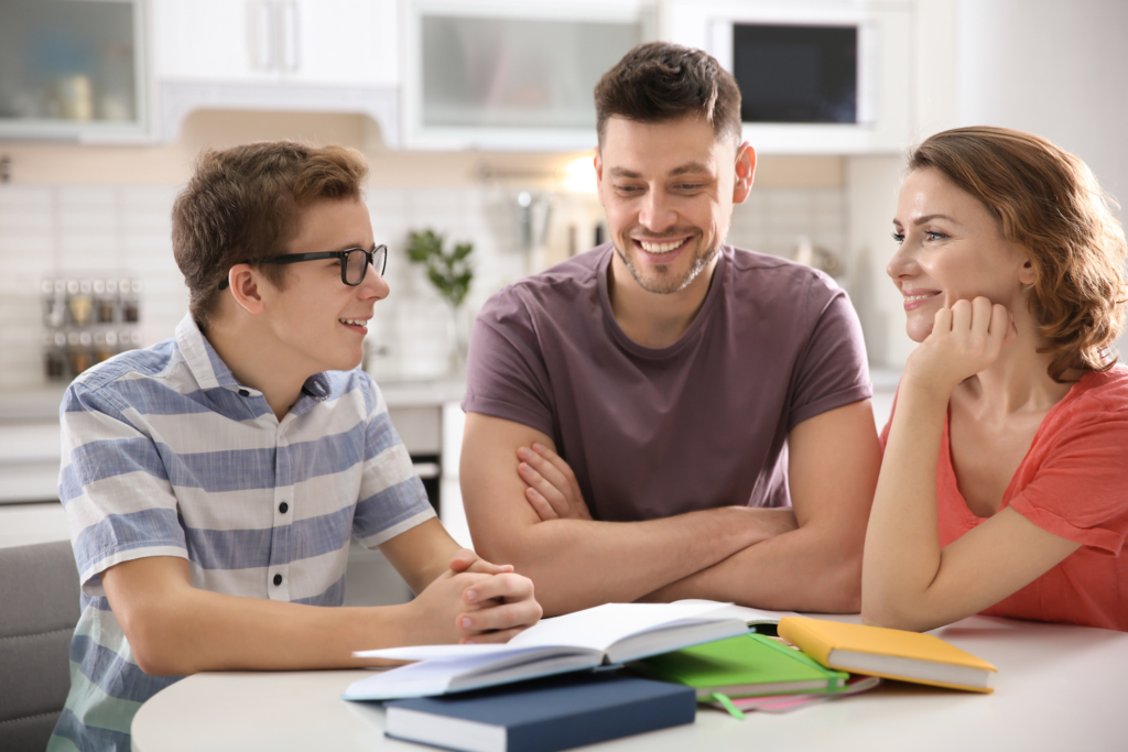 Young teen son at the kitchen table doing homework with help from his Dad and Mom.