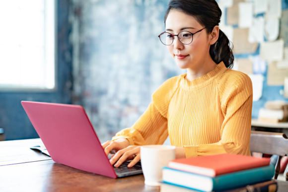 Bespectacled woman sitting down, typing on a laptop.