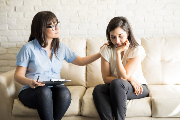 Professional woman with a clipboard comforting a young woman.