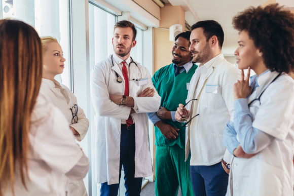 Team of doctors and nurses huddled together talking.